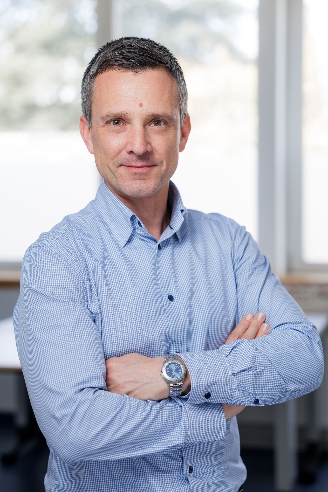 Portret moškega s prekrižanimi rokami v svetlomodri srajci v pisarniškem prostoru.