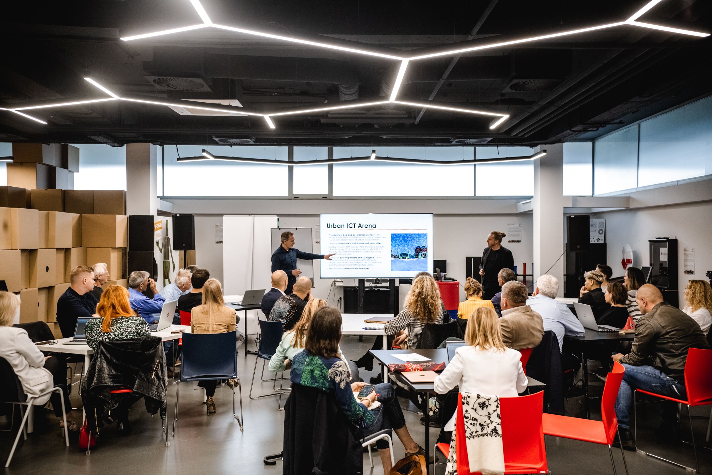 Fotografija moškega med predstavitvijo ter skupine poslušalcev, ki pozorno poslušajo.