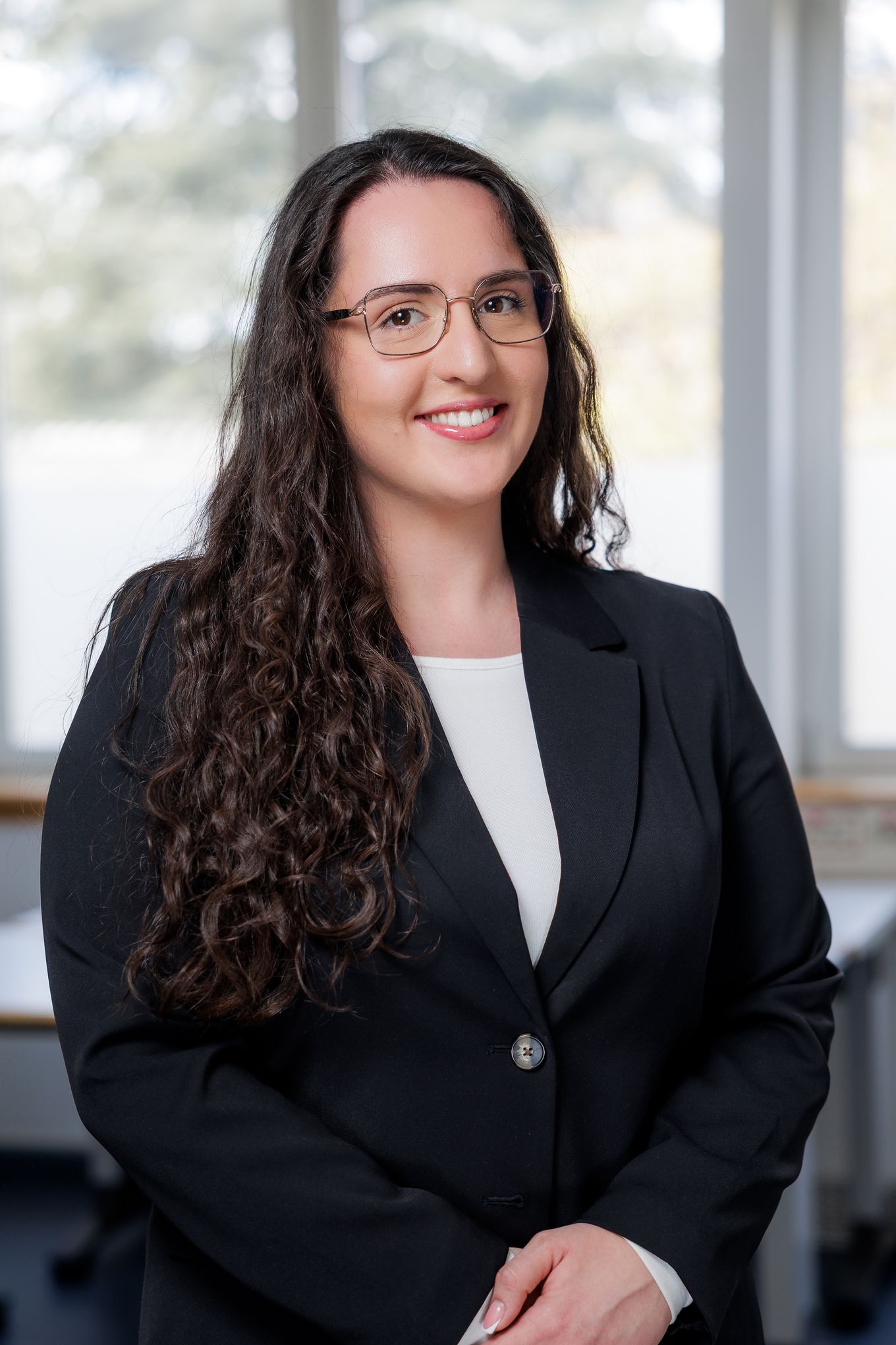 Portret nasmejane ženske z očali in dolgimi temnimi lasmi v temnem suknjiču.